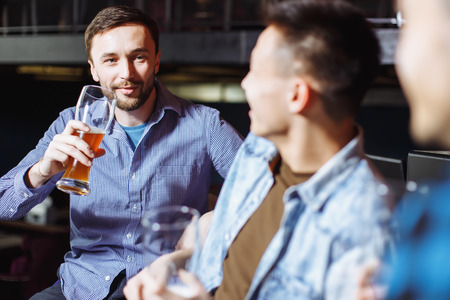 People, men, leisure, friendship and celebration concept - happy male friends talking and drinking beer at bar or pub.の写真素材