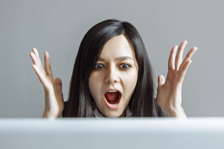 Stressed shocked business woman sitting at table in front of laptop looking stunned wide open mouth.