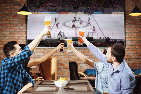 Group of young men cheering on their favorite hockey team watching the game on TV at the local pub having beer.の写真素材