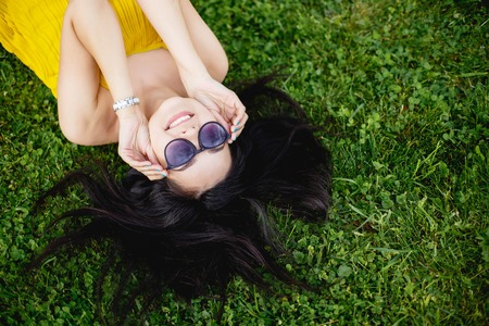 Happy young brunette woman in sunglasses lying on the grass, top view.の写真素材