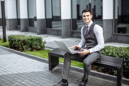 Portrait of a successful young man working on laptop on bench outdoorsの写真素材