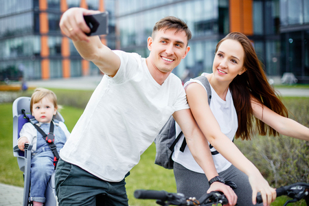 A happy family makes selfie on a smartphone while walking on bicycles in the summer.の写真素材