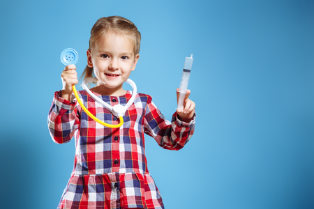 Kid girl playing doctor with syringe and stethoscope on a blue backgroundの写真素材