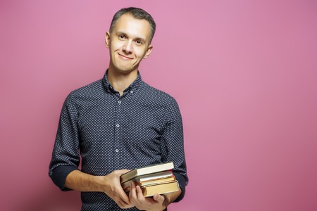 Young man holding a stack of books on a pink backgroundの写真素材