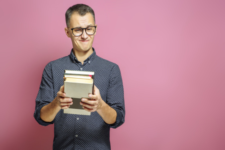 Surprised man with a stack of books on a pink background.の写真素材