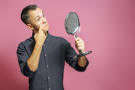 Surprised young man looking in mirror on pink backgroundの写真素材