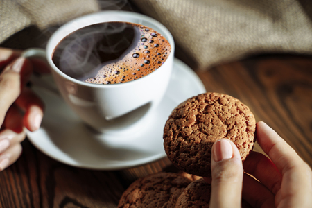 Female hands holding cup of coffee and cookie on wooden table close upの写真素材