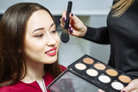 Makeup artist applying powder on the face of the woman in make up room.の写真素材