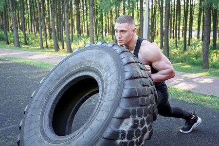 Strong young man flipping tyre while exercising outdoor. CrossFitの写真素材