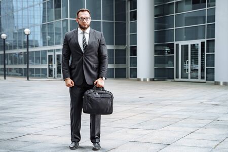 Portrait of a business man in a suit with a bag in his hands on the street.の写真素材
