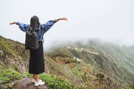 Young woman tourist with backpack relaxing on top of a mountain and enjoying the view of valley.の写真素材