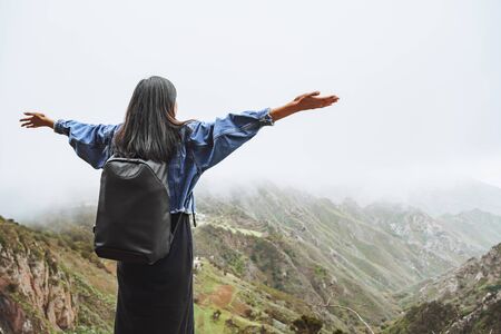 Young woman tourist with backpack relaxing on top of a mountain and enjoying the view of valley.の写真素材
