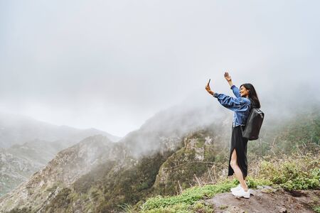 Happy woman tourist taking selfie using smartphone on top of a mountain.の写真素材