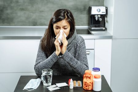 Sick woman with medicine blowing nose to paper wipe at home.の写真素材