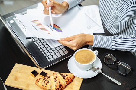 Coffee, croissant and female hands holding documents on the desktop. Business breakfast concept.の写真素材