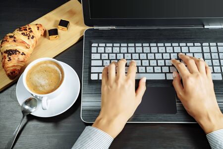 Coffee, croissant and female hands on a laptop keyboard. Business breakfast conceptの写真素材