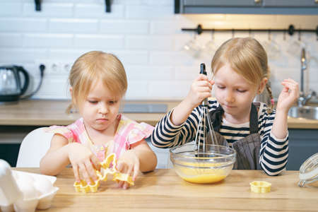 Two cute sisters preparing cookie dough. Little girls helping mom in the kitchen.の写真素材