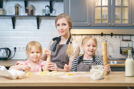 Portrait of a happy family mom and two cute daughters preparing homemade cookies in the kitchen.の写真素材