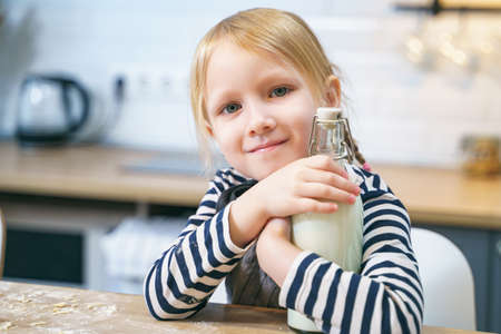 Portrait of a smiling cute girl holding a bottle of milk in the kitchen.の写真素材