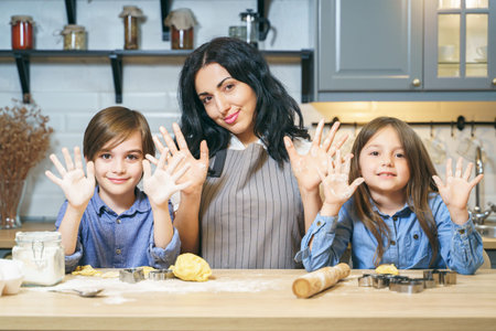 Portrait of a happy family of mom and two children showing hands and smiling while preparing cookies...