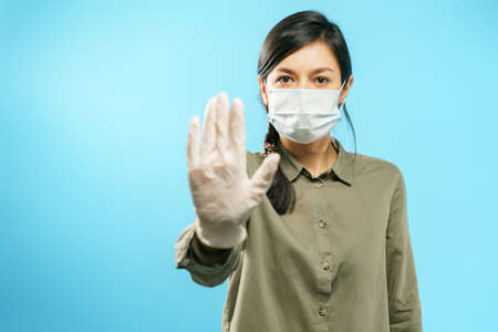 Portrait of a young woman in protective medical mask and gloves showing stop gesture. Social distancing and individual protection during the coronavirus pandemicの写真素材