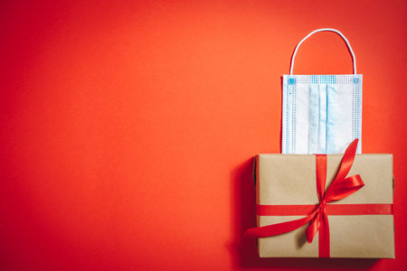 Gift box with ribbon and medical protective mask on red background. Copy space.