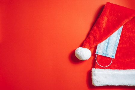 Close-up of Christmas santa hat and medical mask on a red background. New year and pandemic concept.