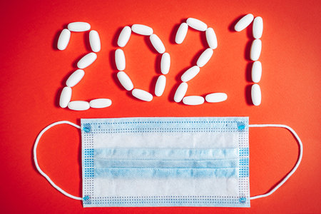 Medical mask and numbers 2021 from pills on red background.の写真素材