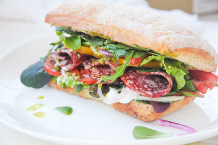 Burger ciabatta with smoked sausage and salami, fresh salad mix, tomatoes, pesto sauce and onionsの写真素材