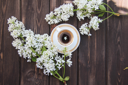 a Cup of coffee and a branch of lilacs on a wooden tableの写真素材