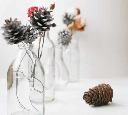 home decoration of glass bottles, Christmas tree cones and dried flowers on white tableの写真素材