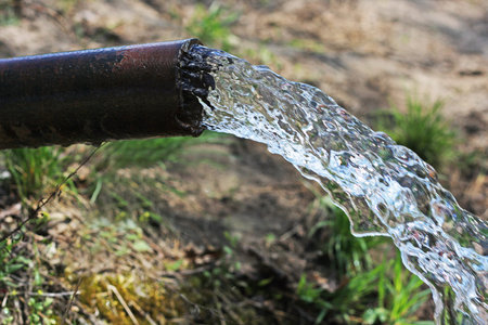 Old rusty pipe close-up, from which flows a strong stream of water.
