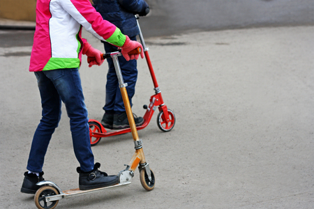Two teenagers ride on Kick scooter by asphalt road.の写真素材