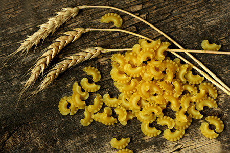 Ears of wheat on a brown wooden background. Near the scattered ears of wheat pasta.の写真素材