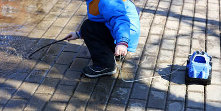 Walk in the spring. Children play in the fresh air. The child sits on his haunches near the large puddles.In the hands of the child a rope from a toy car.の写真素材