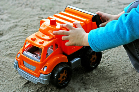 Children's sand games. The child sits near a large toy car. Hands of the child close-up.