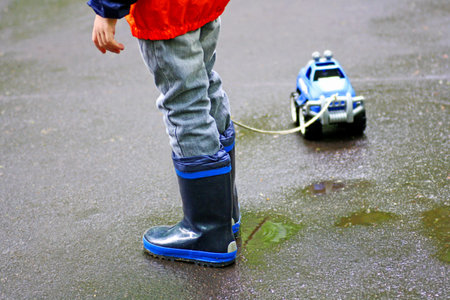 Children walk in autumn. The boy walks in puddles. In the hands of the child the rope from the toy car.の写真素材