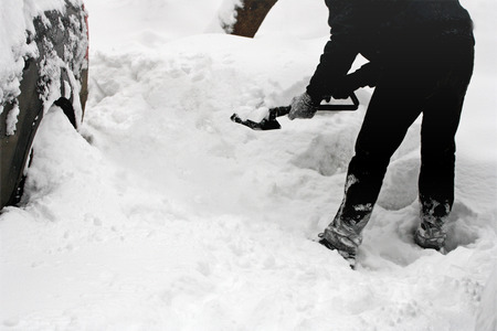 Snowy winter. A man with a shovel digging out the car from snow.の写真素材