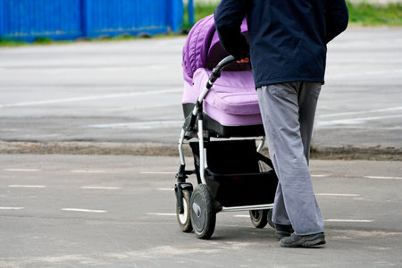 Walking father with child in the fresh air. A man carries a baby stroller on a paved road.の写真素材