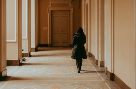 Woman in bright corridor in black coatの写真素材