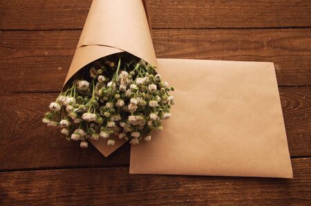 Bouquet of camomile field wrapped in kraft paper on a wooden tableの写真素材