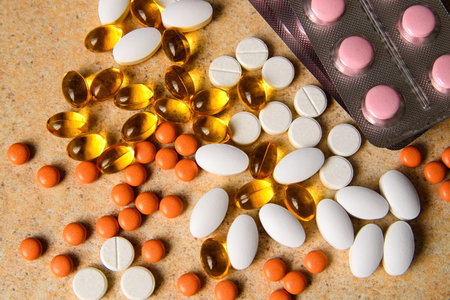 Blister with pink and orange pills, vitamin D and fish oil capsules randomly lie on sand background...