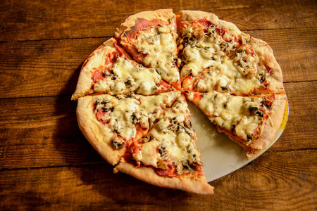 pizza cooked at home-made is cut into pieces and lies on a wooden tableの写真素材