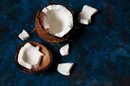 Open coconut lies on a dark blue background next to broken pieces lying randomlyの写真素材