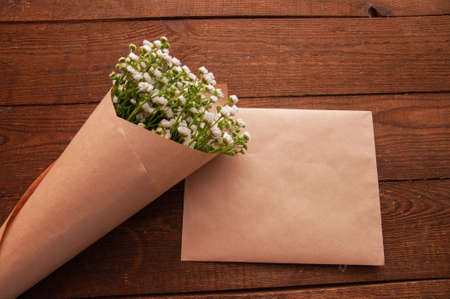 envelope made of craft paper, next to a bouquet of chamomile flowers, which lies on a wooden tableの写真素材
