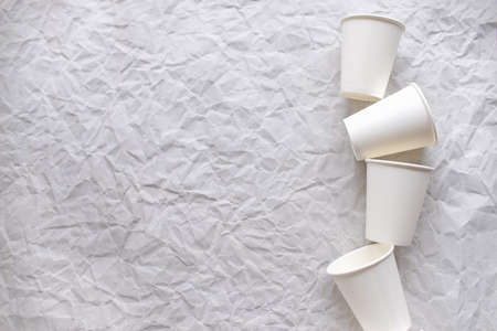 disposable cups made of white paper are laid out on gray crumpled paper in a geometric patternの写真素材