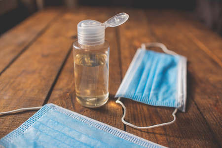 plastic bottle with hand sanitizer and disposable masks lie on a wooden tableの写真素材