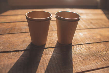 Disposable dark brown kraft paper cups stand on wooden table against brown backgroundの写真素材