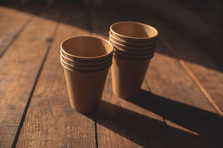 Disposable dark brown kraft paper cups stand on wooden table against brown backgroundの写真素材