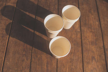 disposable white cardboard cups stand on a wooden table on a brown backgroundの写真素材